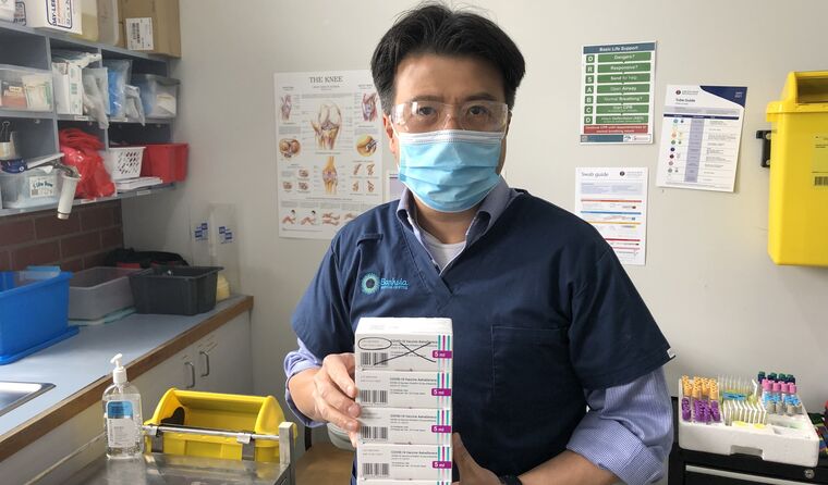 A GP in PPE and holding boxes of AstraZeneca.