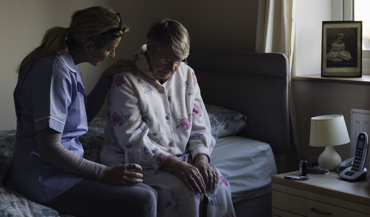 Nurse sitting on bed comforting elderly patient.