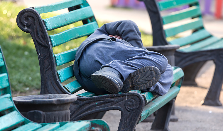 Homeless man sleeping on park bench.