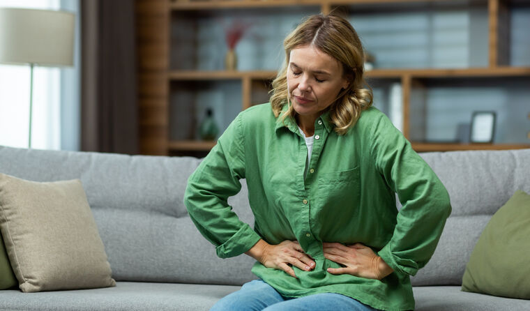 A woman sits on a couch with abdominal pain.