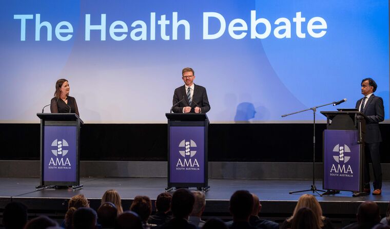 Three people stand on a stage doing a debate.