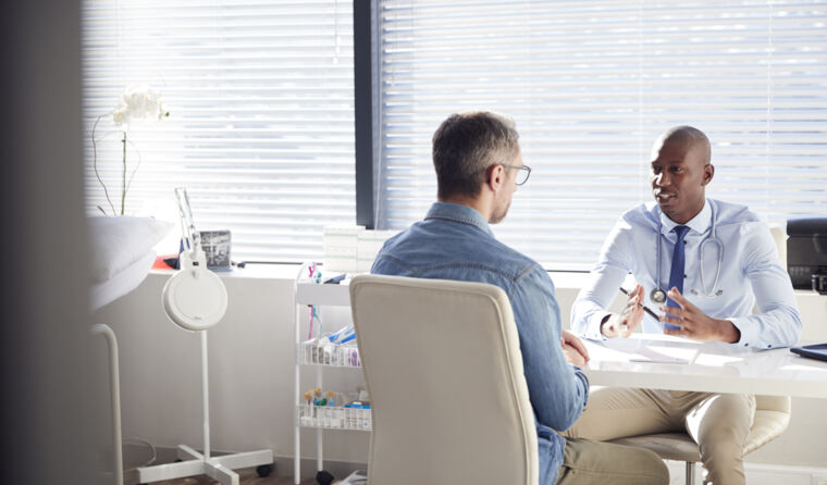 Two male doctors sit at a desk talking.