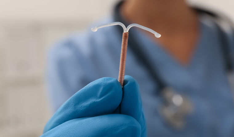 A gloved hand holds up an IUD,