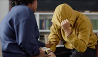 Doctor talking to patient with head in his hands.