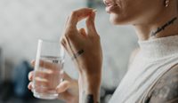 A woman about to take tablet with glass of water.