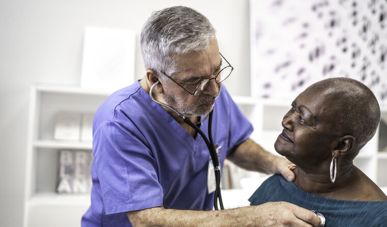 Older male doctor uses stethoscope on female.
