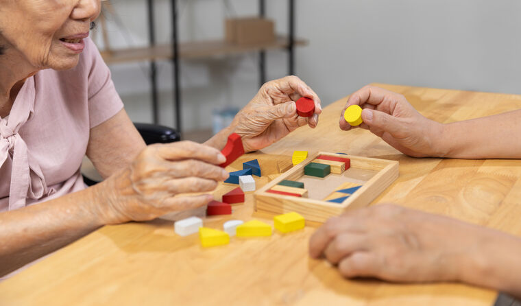Elderly Asian lady playing with wooden blocks toy.