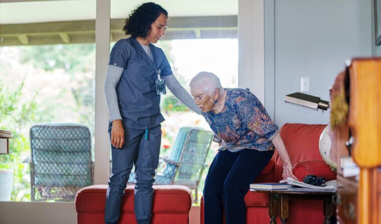 Woman in blue scrubs helps elderly lady get up.