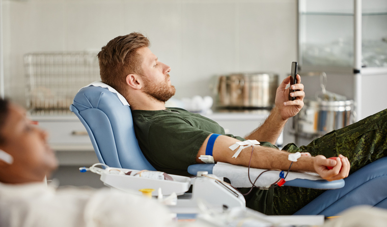 A man using his phone while donating blood.