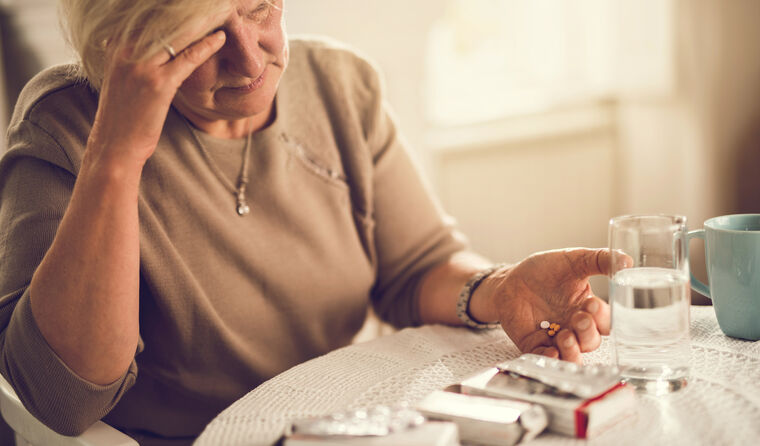 Older women taking medication with head in hands.