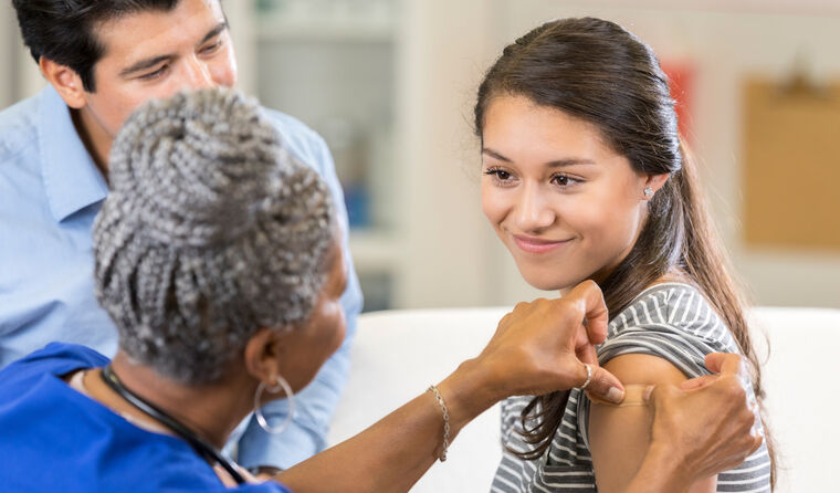 Smiling teenage girl gets vaccination in arm