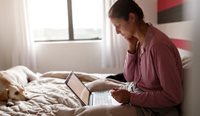 Woman sitting in bed looking at computer.