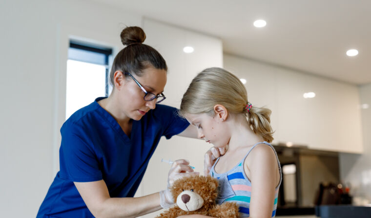 Young girl with teddy bear given vaccination.