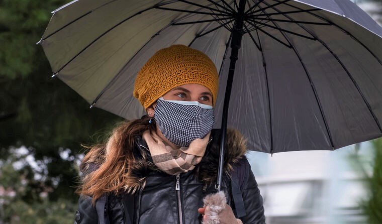 Woman wears a mask and holds an umbrella. 