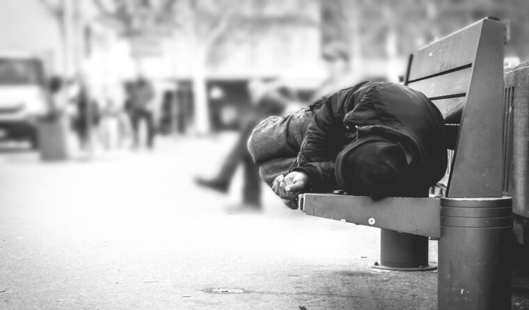A homeless man sleeping on a park bench.