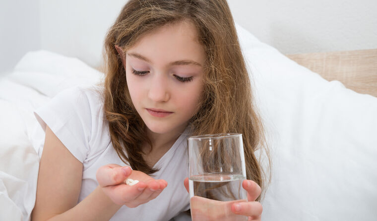 Young girl on a bed with pills and glass of water.