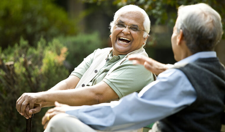 Two elderly men sit outside together, laughing.