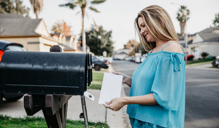 Woman holding a letter at her mailbox.