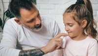 A dad administers a nasal spray to his daughter.