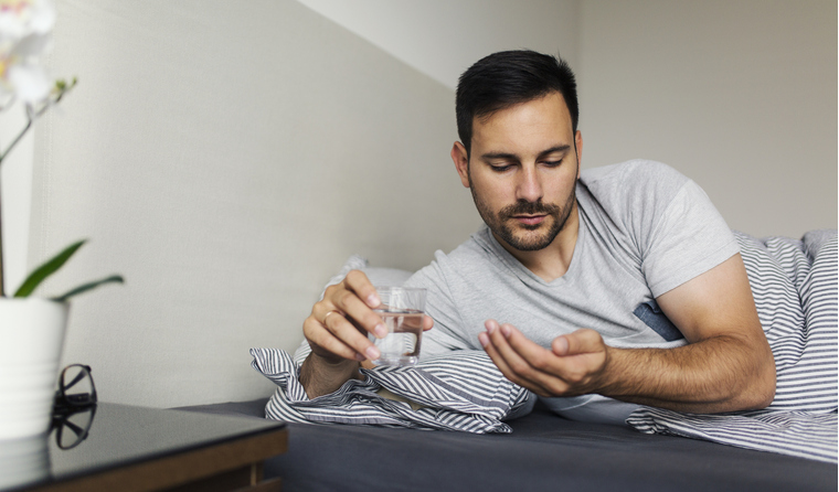A man taking medication while in bed. 