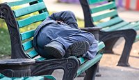 Homeless man sleeping on park bench.