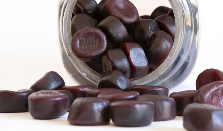 Dark red gummies spill out of a jar onto a table.