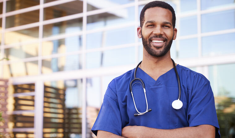 A smiling young male doctor standing outside.