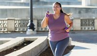 An overweight woman jogs while holding weights.
