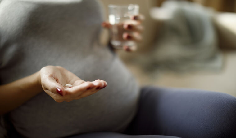 Pregnant woman holds glass of water and pill.