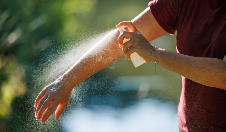 A person sprays insect repellant on their arm.