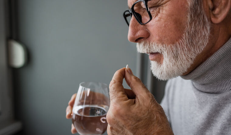 Older man takes small white pill with water