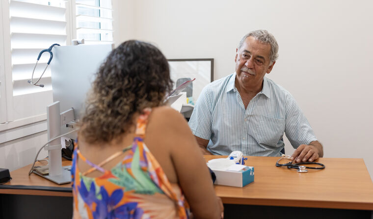 Aboriginal male doctor sits opposite woman at desk