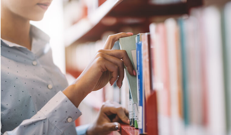Woman reaching for book on library shelf