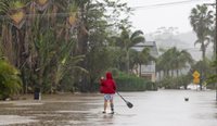 A person uses a paddleboard on a flooded street in Port Macquarie, New South Wales. (Image: AAP/Lindsay Moller)