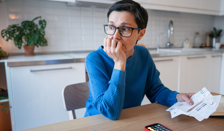 Worried woman at table with bills and calculator.