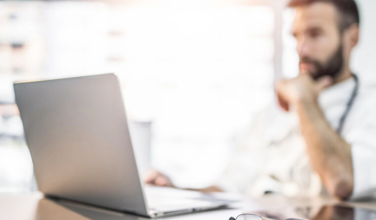 Doctor, blurred into background, sits at computer.