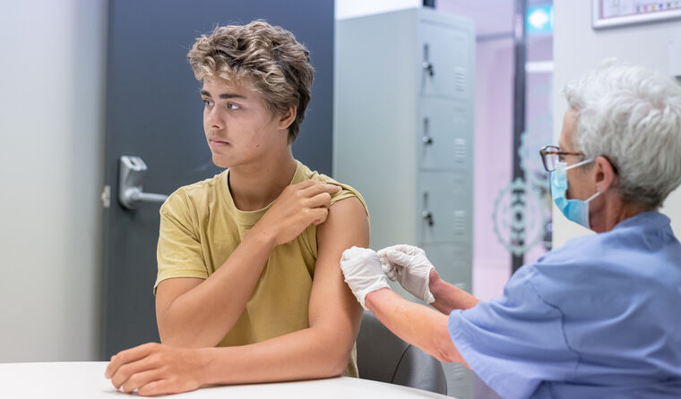 A teenage boy receives a vaccination in his arm.
