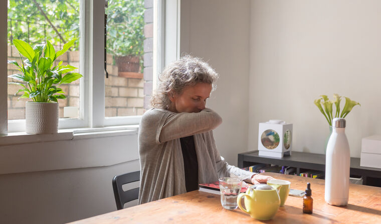 Middle-aged woman sits at table coughing