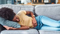 Woman on couch holding stomach in pain