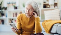 Older pensive woman sits looking at mobile phone
