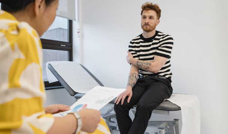 Young man in striped tee sits in doctor's clinic.