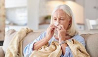 Elderly woman on couch blowing her nose.