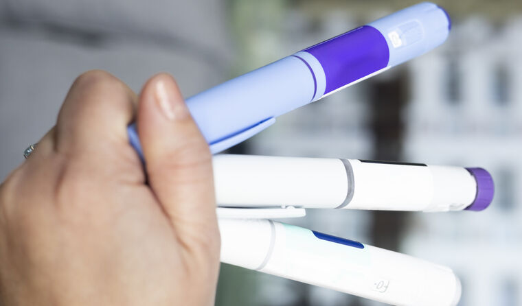 Person holding GLP-1 RA pens.