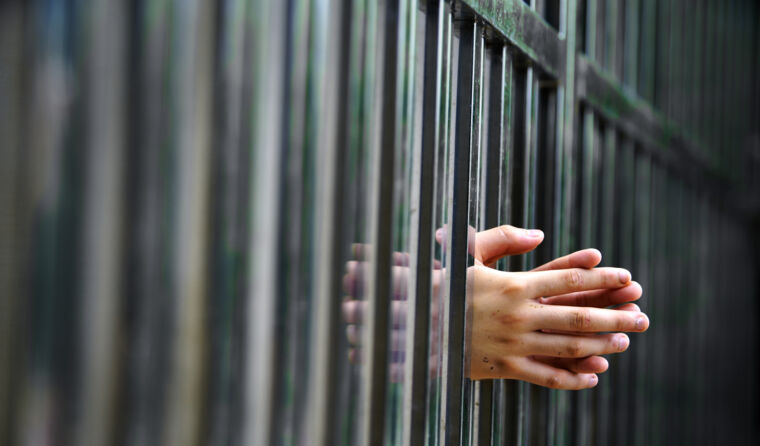 Person's hands on jail bars.