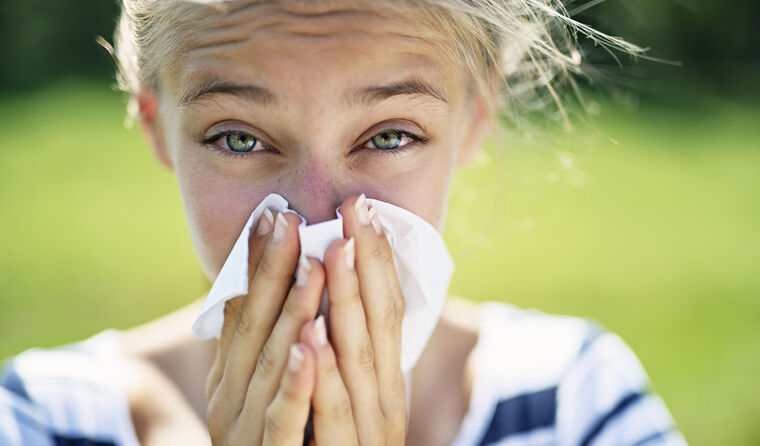 A young woman blows her nose into a tissue.